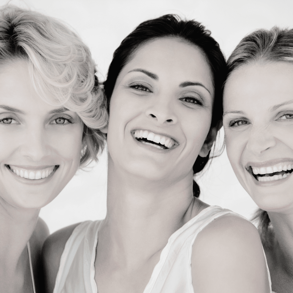 Three women smiling and laughing together, facing the camera closely, with light backgrounds and soft, natural lighting. This joyful moment reflects the confidence often seen after treatments in medycyna estetyczna Wrocław.