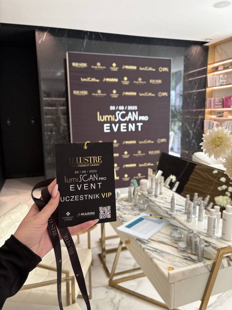 A hand holds a VIP badge for the lumiSCAN PRO EVENT in a modern, elegant room at a klinika medycyny estetycznej, with product displays, gold flowers, and a dark backdrop showcasing event branding.